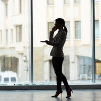 Profile view of unrecognizable businesswoman conducting telephone negotiations while standing at spacious office with panoramic windows