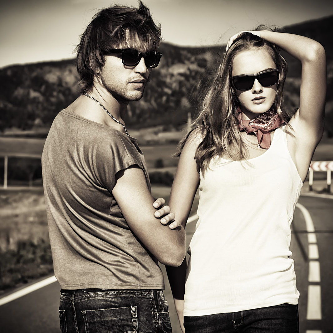 Couple of modern young people posing on a road over picturesque landscape.